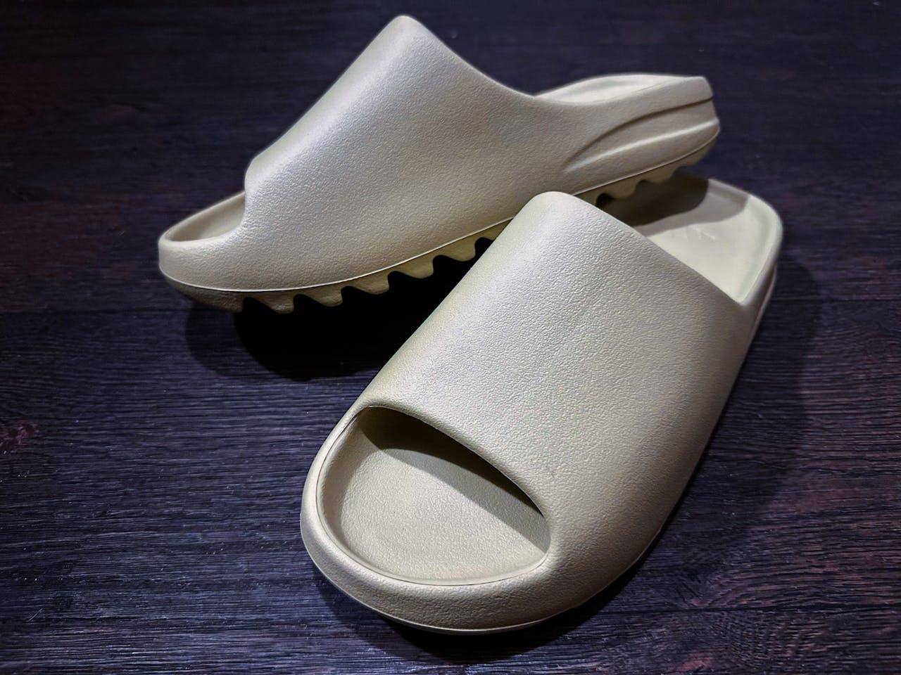 Close-up of trendy beige sandals on a dark wooden surface, highlighting unique minimalist design.