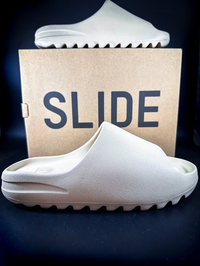Close-up of tan slide sandals in front of labeled box, perfect for fashion contexts.