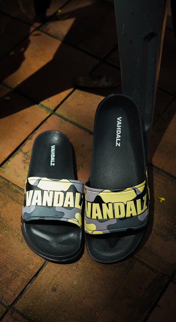 Close-up of fashionable Vandalz slides on a brick patio, showcasing stylish footwear.