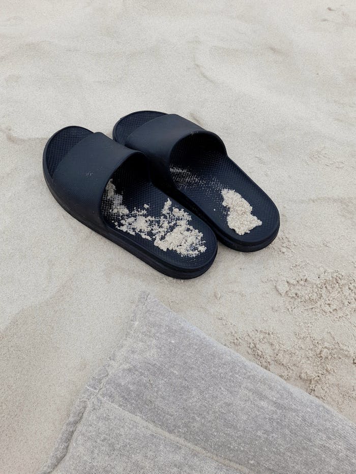 Black slippers on sandy beach capture relaxation and vacation vibes.